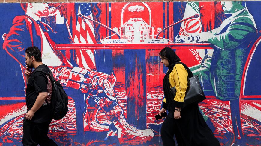 A man and woman walk past a mural depicting an Iranian official in civilian clothing sitting across the table from an American official wearing military fatigues painted on the outer walls of the former US embassy in Tehran, colloquially referred to as the "Spy Den," on April 8, 2025.