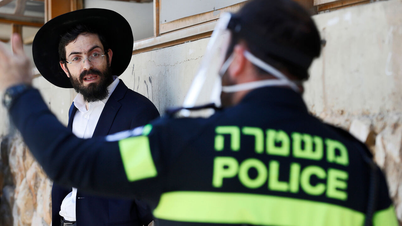 1208944620 An Israeli police officer speaks to an ultra-Orthodox Jewish student at a Yeshiva (Talmudic school) in Bnei Barak, a city east of Tel Aviv with a significant ultra-Orthodox Jewish population, on April 2, 2020, as part of measures imposed by Israeli authorities against the COVID-19 coronavirus pandemic. - Israeli police backed by surveillance helicopters have stepped up patrols of ultra-Orthodox Jewish neighbourhoods that have become coronavirus hotspots. (Photo by JACK GUEZ / AFP) (Photo by JACK GUEZ/AFP vi
